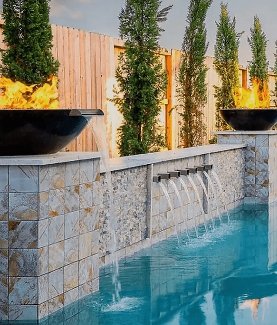 Fire bowls and water scuppers built into a stone pool wall, from The Outdoor Plus fire and water feature range